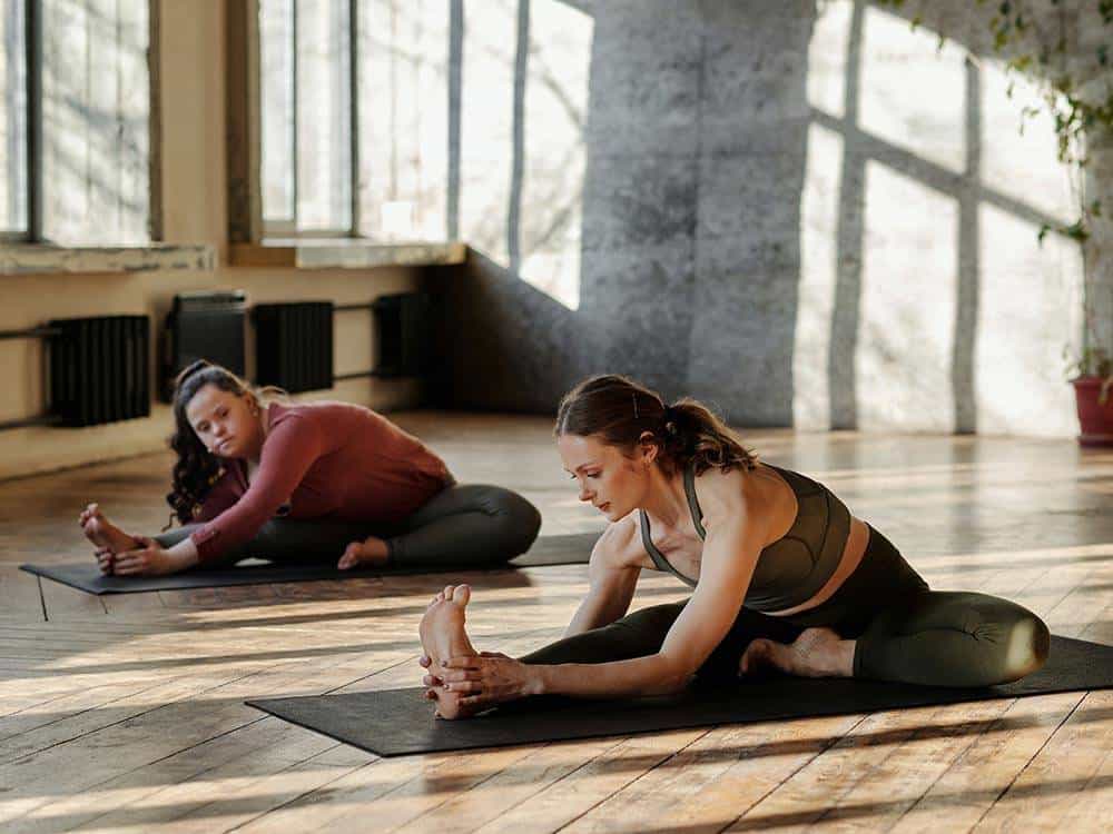Zwei Frauen machen Geburtshelfer-Übungen im Yoga-Studio, entspannte Atmosphäre, natürliche Lichtverh.