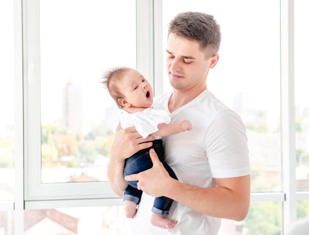 Vater haelt sein Baby am Fenster nach einer belastenden Geburt