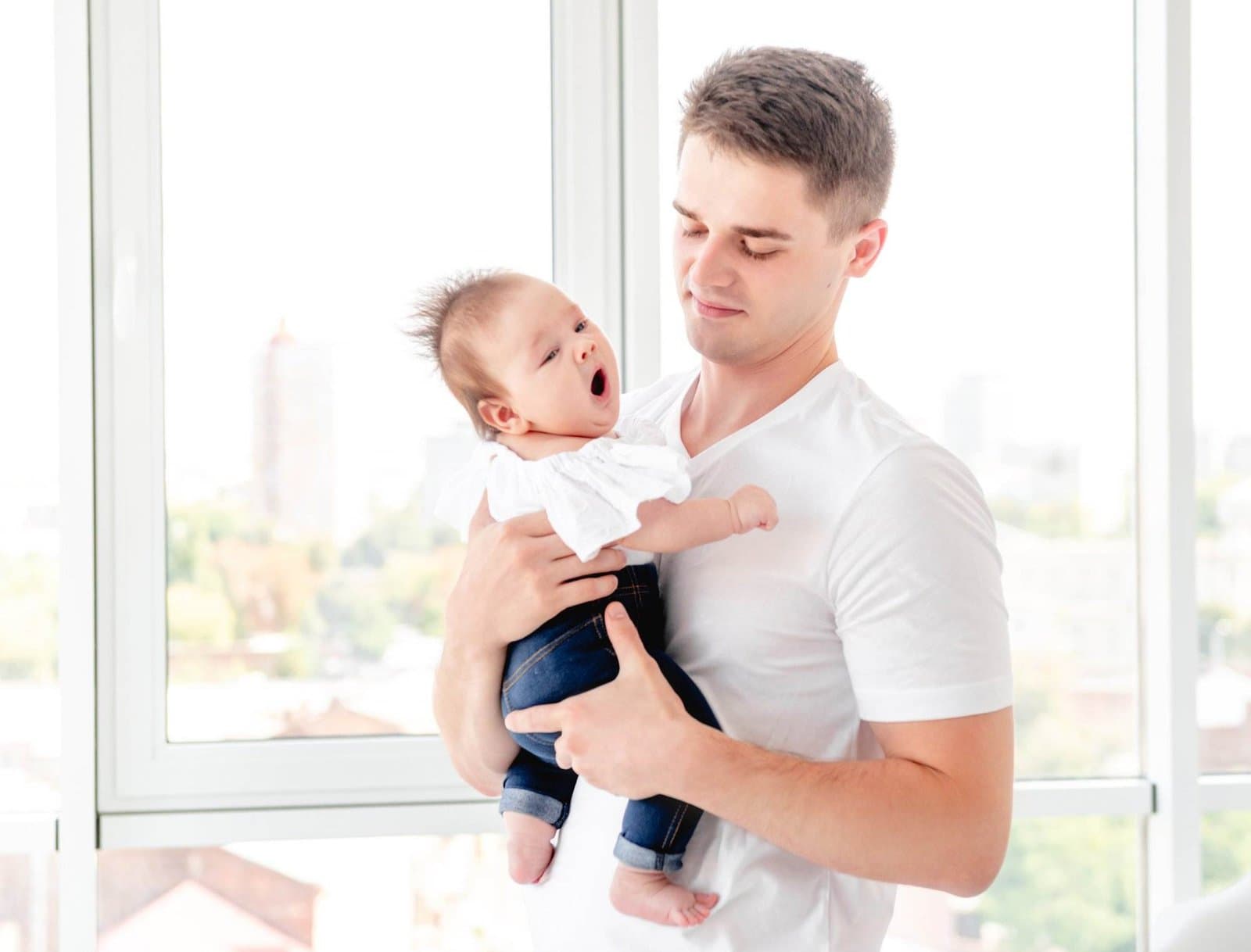 Vater haelt sein Baby am Fenster nach einer belastenden Geburt