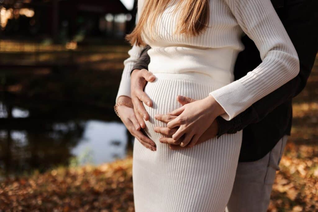 Schwangere Frau mit Partner umarmt Bauch im Park, Natur, Herbst.