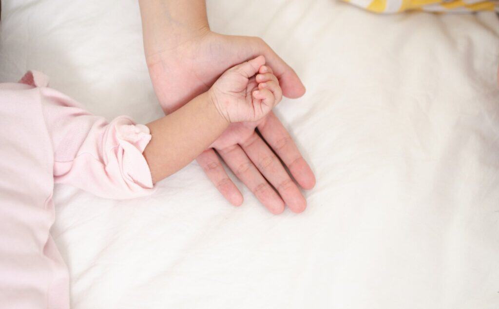 Nahaufnahme einer Babyhand, die eine erwachsene Hand hält, symbolisiert Fürsorge und Geburtshilfe.