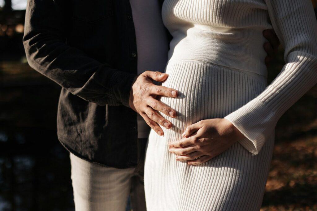Schwangere Frau mit Partner, die ihre Babybauch halten, im Freien bei Sonnenlicht.
