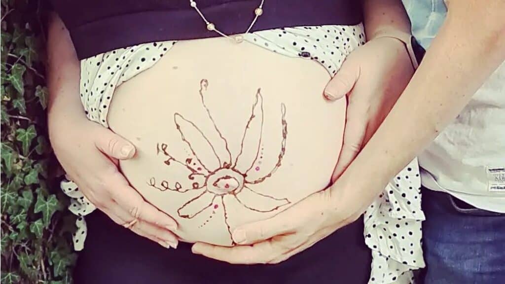 Nahaufnahme eines schwangeren Bauchs mit handgezeichnetem Baby- und Muttermotiv, symbolisiert Geburt.